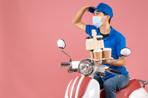 Vue de dessus d'un livreur masculin concentré en masque portant un chapeau assis sur un scooter livrant des commandes sur fond de pêche