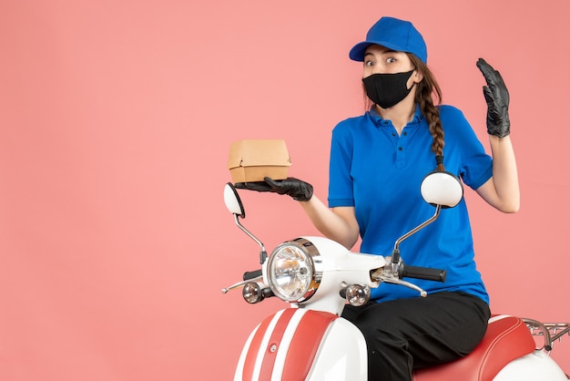 Vue de dessus d'un livreur surpris portant un masque médical et des gants assis sur un scooter livrant des commandes sur une pêche pastel