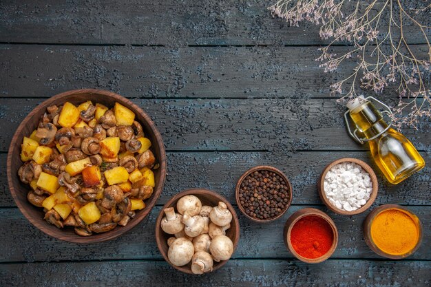 Vue de dessus de loin assiette de nourriture assiette de pommes de terre et de champignons à côté d'un bol de champignons blancs épices colorées et huile en bouteille