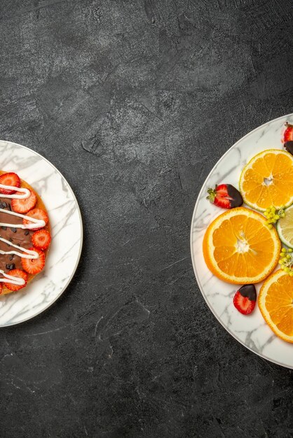 Vue de dessus de loin des assiettes sur le gâteau de table avec du chocolat et des fraises à côté de l'assiette d'agrumes et de fraises enrobées de chocolat