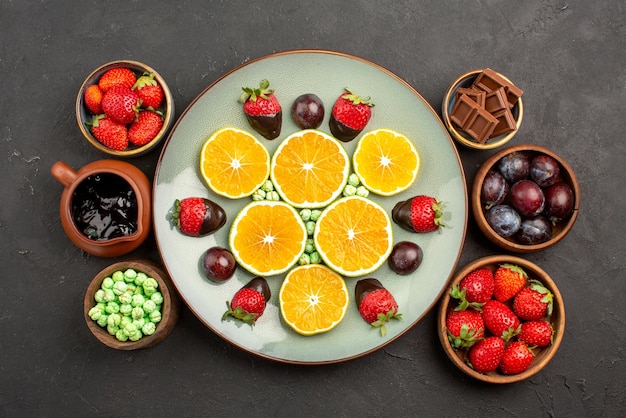 Vue de dessus de loin des baies et une assiette de chocolat de fraises enrobées de chocolat et d'orange hachée à côté des bols de bonbons à la sauce au chocolat et de baies sur la table