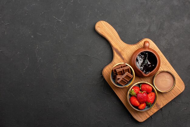 Vue de dessus de loin des bols en bois de dessert de crème au chocolat et de baies sur la planche à découper sur la table sombre