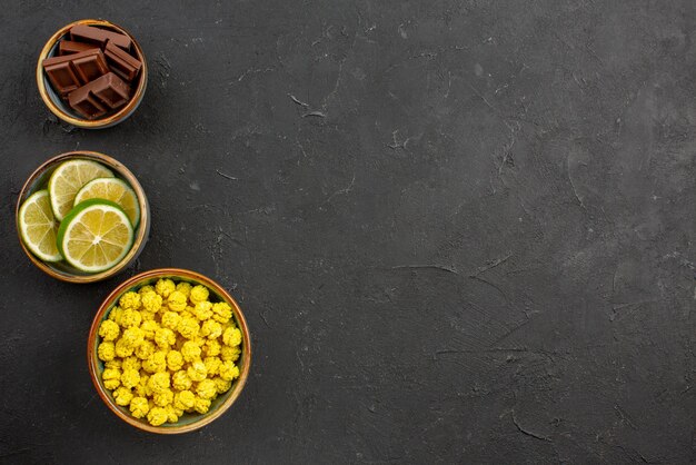 Vue de dessus de loin des bols de bonbons au chocolat et des tranches de citron vert sur le côté gauche de la table