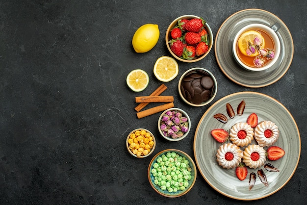 Photo gratuite vue de dessus de loin des bonbons avec des biscuits au thé avec du thé noir à la fraise avec des noisettes de citron des bols de chocolat et différents bonbons sur le côté droit de la table