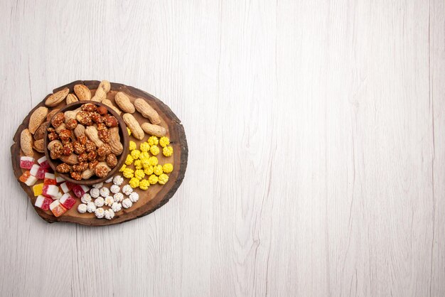 Vue de dessus de loin des bonbons dans un bol de noix sucrées dans un bol à côté des bonbons sur la planche à découper sur le côté gauche de la table blanche