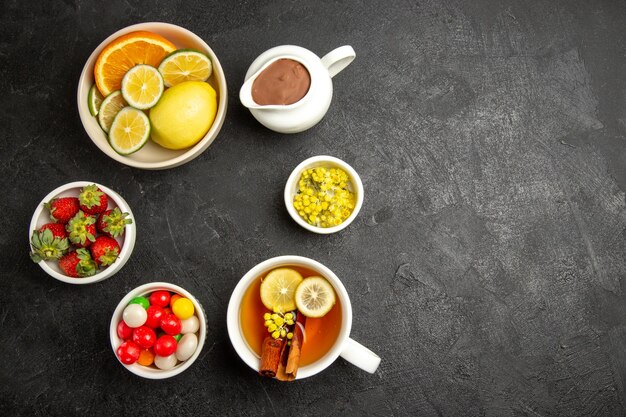 Vue de dessus de loin des bonbons sur la table des bols de fraises et d'herbes et une tasse de thé avec des bâtons de citron et de cannelle