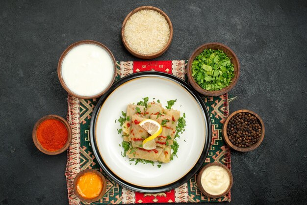 Vue de dessus de loin chou farci chou farci et bols d'herbes sauces blanches et jaunes poivre noir épices riz et crème sure sur nappe à carreaux multicolores sur surface sombre