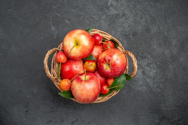 Vue de dessus de loin corbeille de fruits avec des cerises et des pommes sur la table sombre