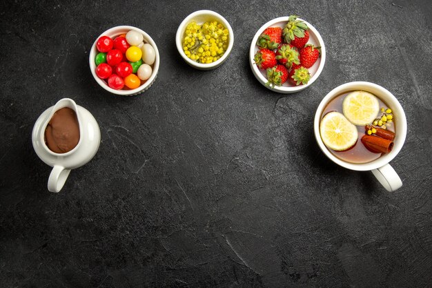 Vue de dessus de loin dessert savoureux quatre bols de bonbons crème au chocolat herbes et fraises et une tasse de thé avec des bâtons de cannelle