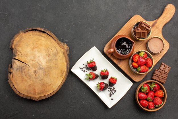 Vue de dessus de loin fraises au chocolat fraises au chocolat chocolat et planche de cuisine avec crème au chocolat et fraises à côté de la planche à découper