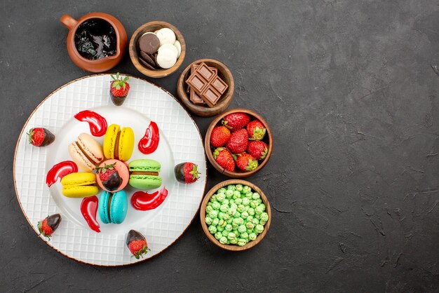 Vue de dessus de loin fraises et macarons assiette de macarons et fraises français appétissants et bols de bonbons autour sur la table