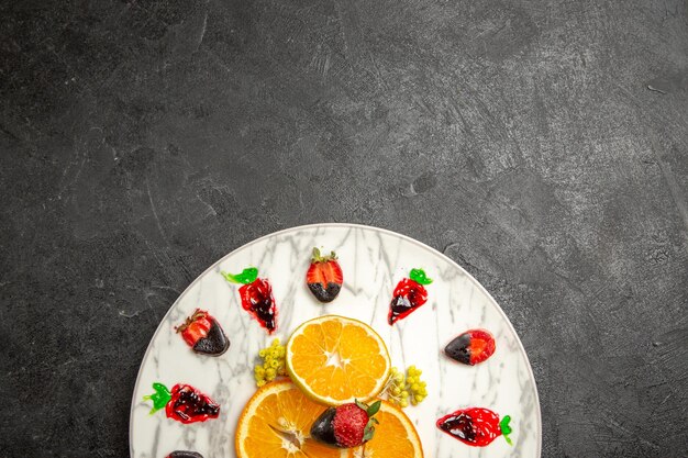 Vue de dessus de loin fruits sur l'assiette tranches d'agrumes et fraises enrobées de chocolat sur l'assiette sur la table sombre