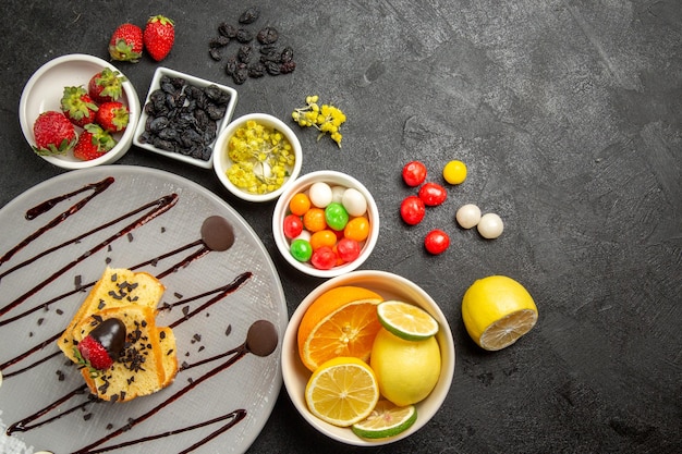 Vue de dessus de loin gâteau aux baies et aux fruits avec des fraises enrobées de chocolat à côté des bols blancs de fraises limes citrons oranges et bonbons colorés sur la table