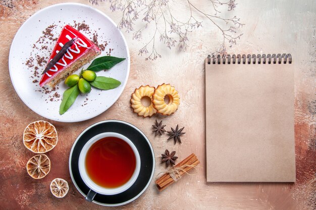 Vue de dessus de loin un gâteau biscuits cannelle une tasse de thé assiette de gâteau crème cahier