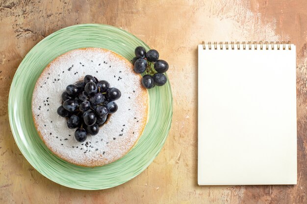 Vue de dessus de loin un gâteau un gâteau appétissant avec cahier blanc de raisins