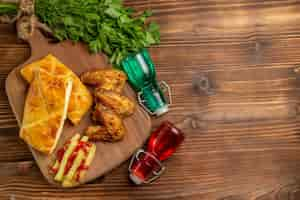 Photo gratuite vue de dessus de loin herbes frites poulet frites et morceaux de tarte sur la planche à découper à côté des bouteilles et des herbes sur la gauche