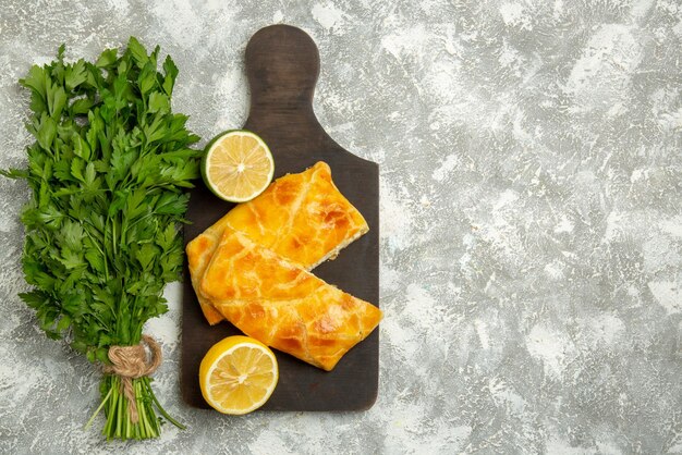 Vue de dessus de loin tartes fines herbes fromage tartes au citron vert et citron sur la planche à découper en bois à côté des herbes sur le côté gauche de la table