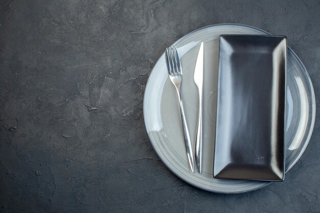 Vue de dessus longue assiette noire avec fourchette et assiette grise sur fond sombre horizontal coloré féminité couverts en verre nourriture