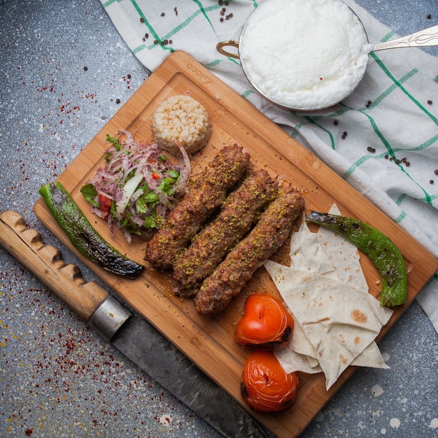 Vue de dessus lula kabab avec légumes frits et oignon haché et couteau et ayran en planche à découper