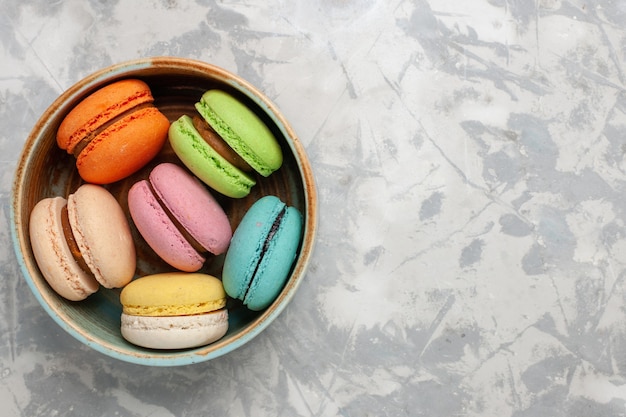 Vue de dessus macarons français colorés délicieux petits gâteaux sur une surface blanche