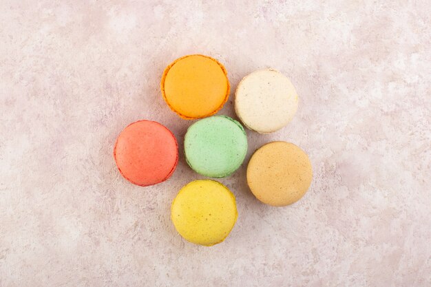 Une vue de dessus des macarons français colorés formés de délicieux sur le gâteau de bureau rose biscuit sucre sucré