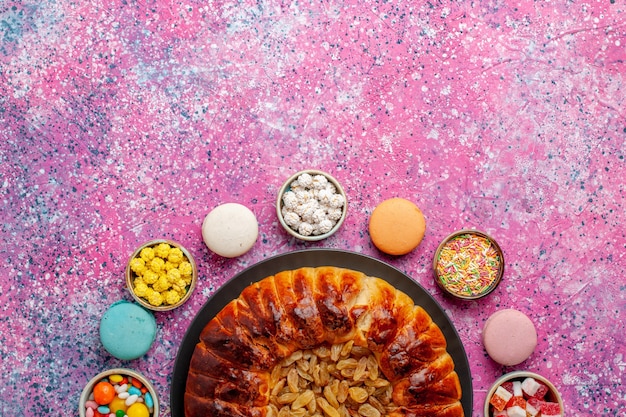 Vue de dessus macarons français colorés petits gâteaux délicieux avec des bonbons et tarte aux raisins secs sur le bureau rose biscuit biscuit gâteau tarte au sucre