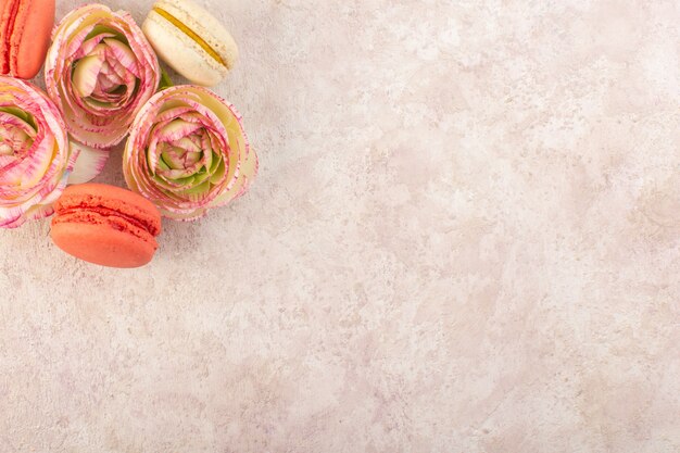 Une vue de dessus macarons français colorés avec des roses fanées sur le gâteau de bureau rose biscuit au sucre sucré