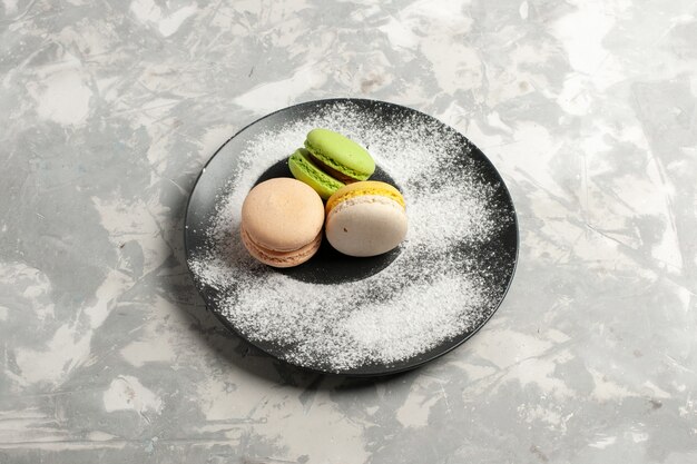 Vue de dessus macarons français délicieux gâteaux colorés à l'intérieur de la plaque sur la surface blanche gâteau biscuit tarte thé sucre biscuits sucrés