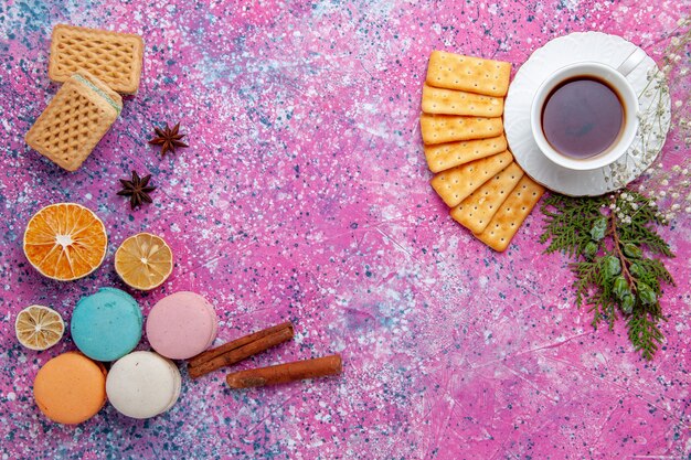 Vue de dessus macarons français avec des gaufres craquelins et tasse de thé sur le bureau rose