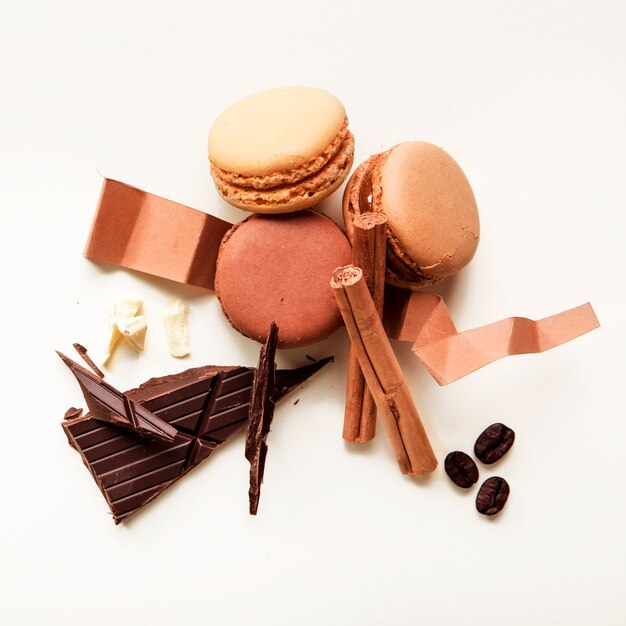 Vue de dessus des macarons; grains de café torréfiés; cannelle et barre de chocolat sur fond blanc