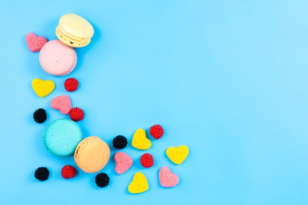 Une vue de dessus macarons et marmelades gâteaux et bonbons français colorés isolés sur le gâteau sucré de sucre de fond de couleur bleue