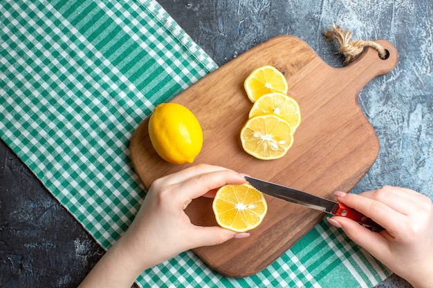 Vue de dessus d'une main coupant des citrons frais sur une planche à découper en bois sur fond sombre