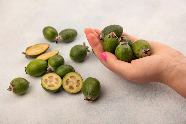 Vue de dessus de la main féminine tenant de délicieux feijoas frais avec des feijoas isolés sur un mur gris