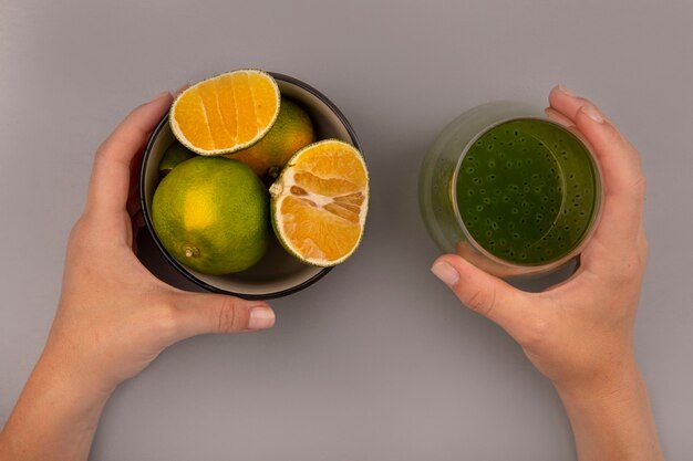 Vue de dessus de la main féminine tenant un verre de jus de kiwi frais dans une main et dans l'autre main un bol avec des mandarines