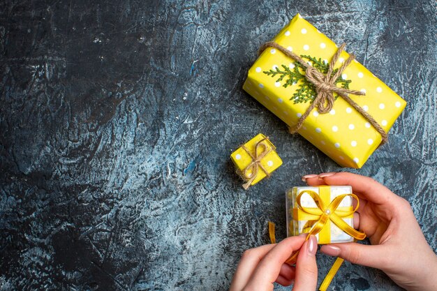 Vue de dessus de la main ouvrant un petit coffret cadeau et deux autres coffrets cadeaux de Noël sur fond sombre