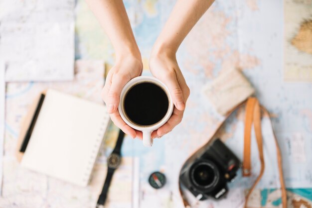 Vue de dessus de la main d&#39;une personne tenant une tasse de café sur la carte de voyage monde floue