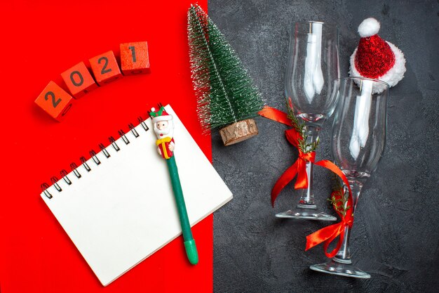 Vue de dessus de main tenant le cahier à spirale et les numéros de gobelets en verre de sapin de Noël sur fond sombre et rouge