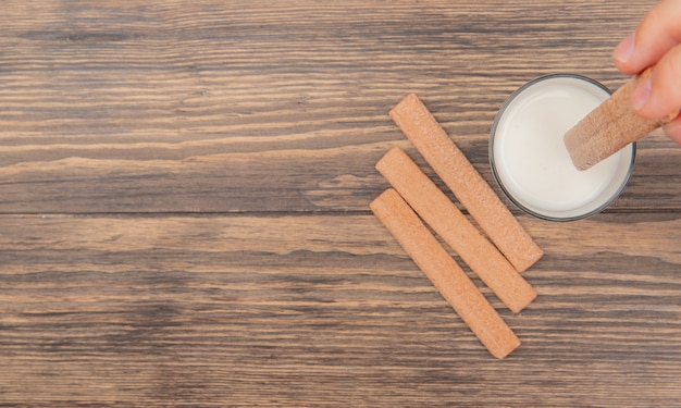 Vue de dessus de la main tenant cookie avec verre de lait et biscuits sur fond de bois avec espace copie