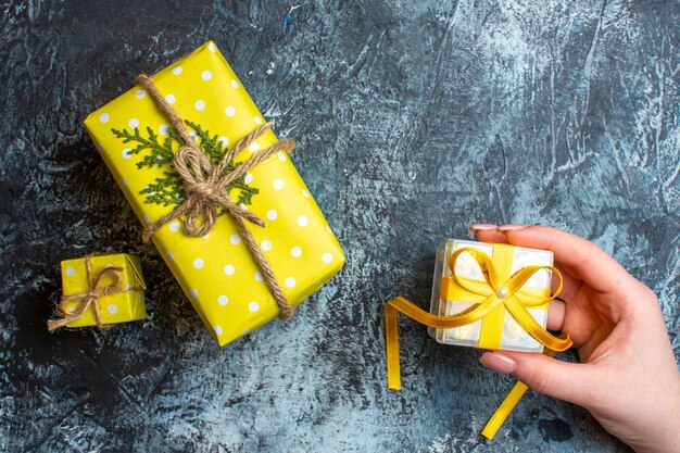 Vue de dessus de la main tenant un petit coffret cadeau et deux autres coffrets cadeaux de Noël sur fond sombre