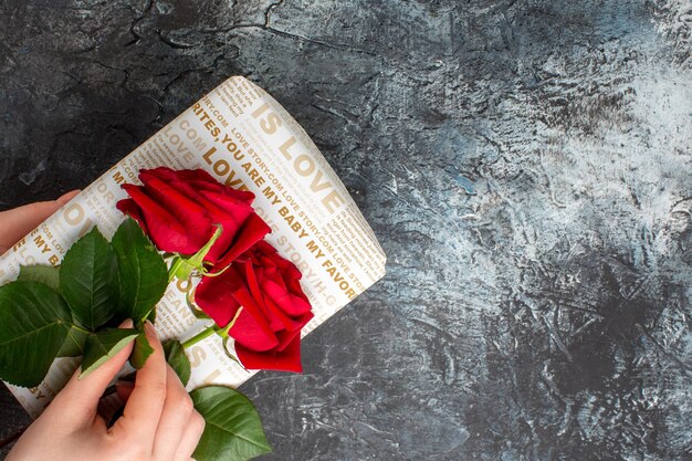 Vue de dessus de la main tenant des roses rouges sur une belle boîte-cadeau sur fond sombre glacial avec espace libre