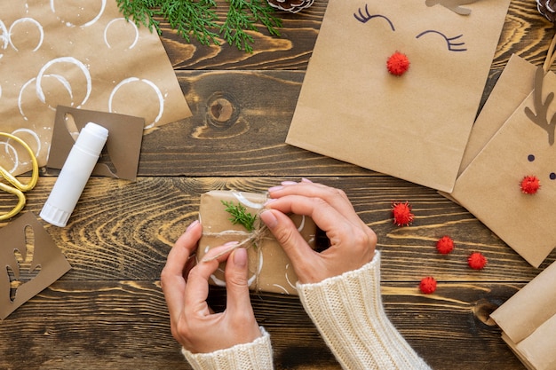 Vue de dessus des mains attachant le cadeau de Noël avec de la ficelle et des plantes