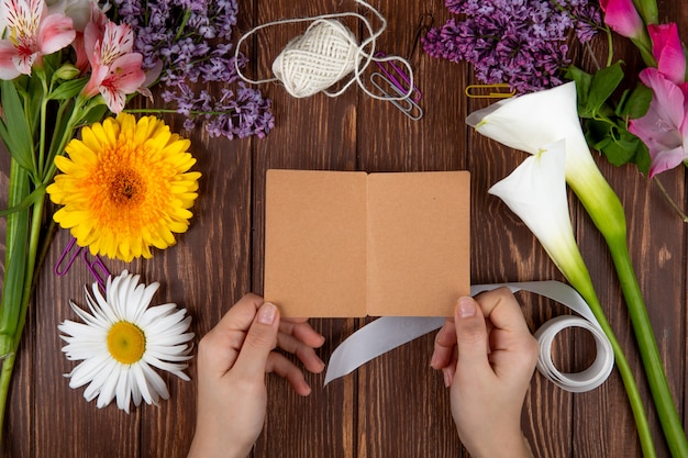 Vue de dessus des mains avec une carte postale et diverses fleurs de printemps gerbera daisy alstroemeria et fleurs lilas sur fond de bois