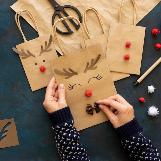 Photo gratuite vue de dessus des mains décorant des sacs en papier de noël avec un renne mignon