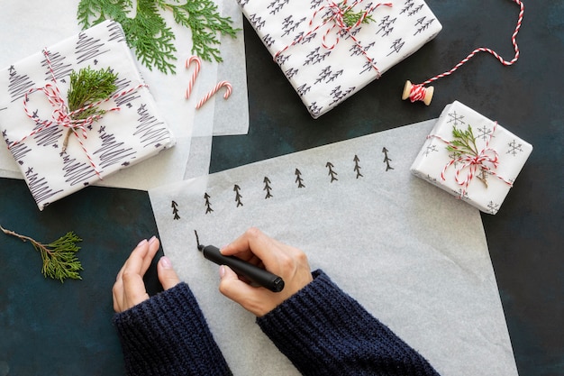 Vue de dessus des mains dessinant des arbres de Noël sur du papier d'emballage