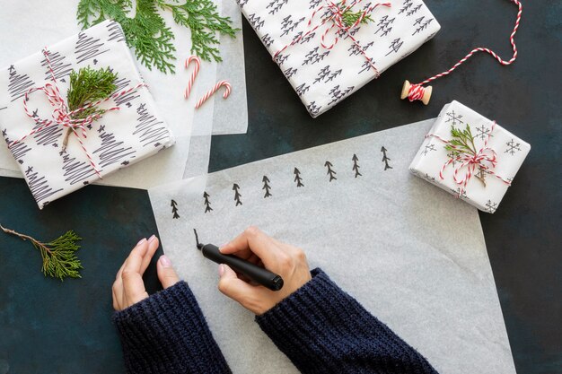 Vue de dessus des mains dessinant des arbres de Noël sur du papier d'emballage