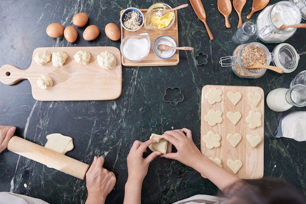 Vue de dessus des mains de deux personnes préparant ensemble des biscuits maison