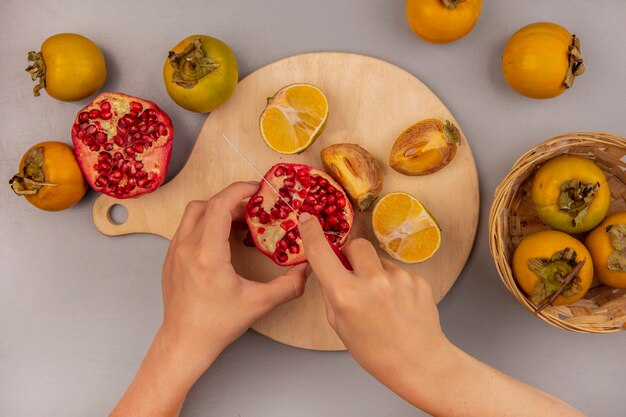 Vue de dessus des mains féminines couper les fruits de la grenade sur une planche de cuisine en bois avec un couteau