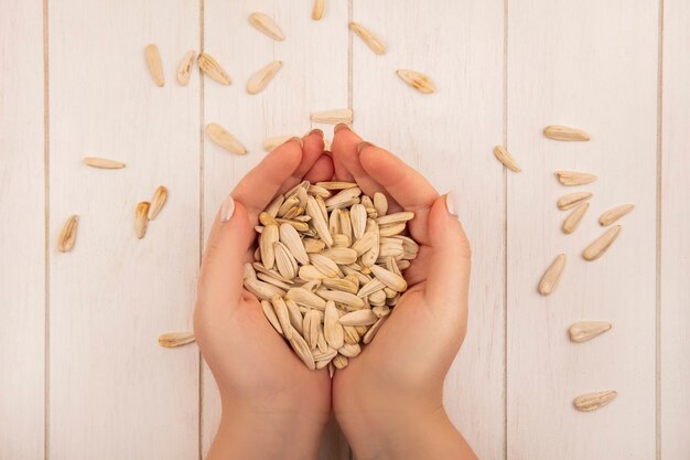 Photo gratuite vue de dessus des mains féminines tenant de savoureuses graines de tournesol blanc salé sur une table en bois beige