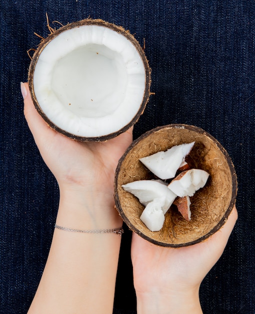 Vue de dessus des mains de femme tenant la noix de coco à moitié coupée avec des tranches de noix de coco en coque sur un tissu de jeans