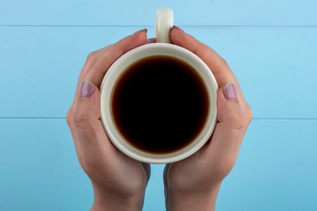 Vue de dessus des mains de femme tenant une tasse de thé sur fond bleu